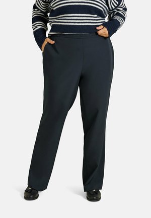Personne portant un pantalon noir à jambes larges, les mains dans les poches, et un pull rayé bleu marine et blanc.