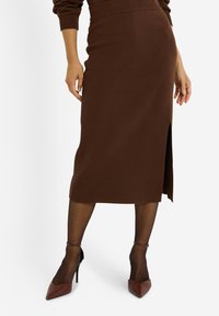 Falda midi de punto marrón con una abertura lateral, combinada con tacones de punta marrón. La textura es suave, con una silueta ajustada.