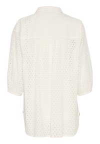 Chemisier blanc avec une texture à pois, des manches bouffantes courtes et un détail de yoke au dos. Le matériau est léger et aéré.
