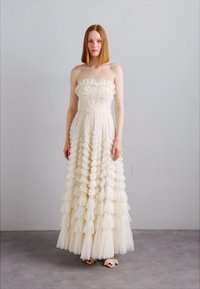Robe ivoire sans bretelles avec un tissu texturé et des volants superposés, descendant d'un corsage ajusté jusqu'à une jupe longue.