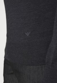 Pull en maille marine avec poignets et ourlet côtelés, présentant un détail discret du logo dans le coin inférieur, mettant en valeur une texture douce et une coupe ajustée.