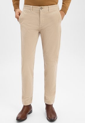 Beżowe spodnie sztruksowe o pionowej, prążkowanej fakturze, wąskim kroju, zapięciem na guziki i bocznymi kieszeniami, w połączeniu z brązowymi skórzanymi butami.