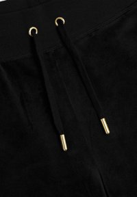 Black sweatpants feature a soft, velvety texture with a drawstring closure. The eyelets and tips are gold-toned for added detail.