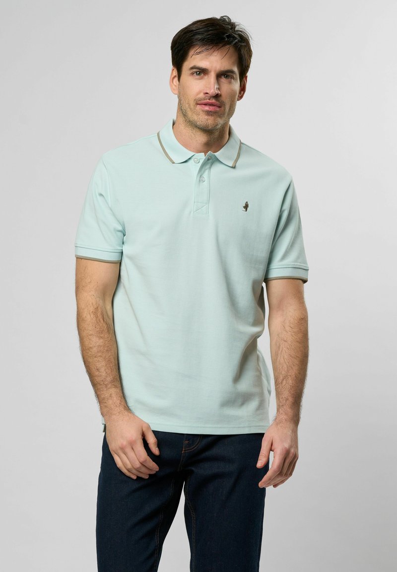 Ljust blå polo skjorta i texturerat tyg, med en krage med kontrasterande kant och en liten broderad logotyp på bröstet.