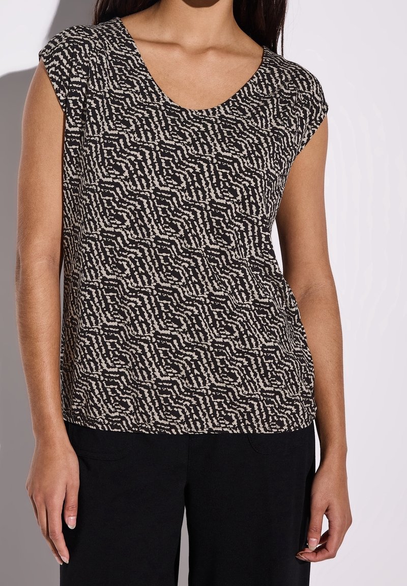 Černý a krémový vzorovaný top s kulatým výstřihem a krátkými rukávy, vyrobený z texturované tkaniny. V kombinaci s černými kalhotami.