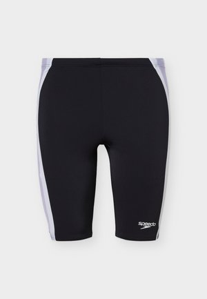 Μαύρο μαγιό μέχρι το γόνατο με λευκές πλευρικές ρίγες και μικρό λευκό λογότυπο Speedo στο αριστερό πόδι, σε απλό φόντο.