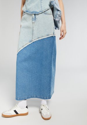 Gonna di jeans con design color block, sezioni blu chiare e scure, orlo sfilacciato, abbinata a sneakers bianche e calzini.