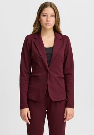 Bordeaux blazer van rekbaar materiaal, met een reverskraag, twee voorzakken en een aansluitend ontwerp. Draag het over een zwarte top.