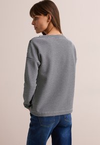 Sweatshirt à manches longues rayé noir et blanc avec une coupe décontractée. Doté d'un col rond et d'une texture douce, associé à un jean en denim bleu.