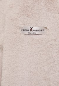 Jasno beżowy materiał z sztucznego futra o miękkiej teksturze, z wyraźnie przymocowaną etykietą z napisem "FRIEDA FREDDIES NEW YORK".