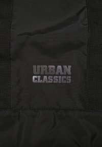 Tela negra con una textura suave que presenta el texto "URBAN CLASSICS" en letras negritas. El diseño es minimalista sin patrones adicionales.