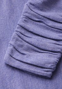 Lila stickad tyg med en texturerad, rynkad ärmdetalj. Mjukt och stretchigt material med subtil färgvariation.