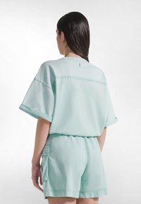 Miętowo zielona, oversize'owa koszula z krótkimi rękawami i okrągłym dekoltem, w zestawie z dopasowanymi szortami. Oba elementy mają gładką, miękką teksturę.