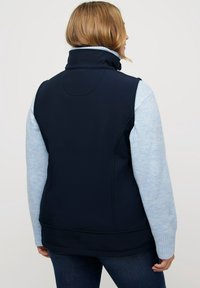 Marineblauer Weste aus weichem Stoff, mit hohem Kragen, figurnahem Design und hellblauen Pulloverärmeln mit gerippten Bündchen.
