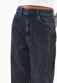 Ciemnoniebieskie dżinsy z wysokim stanem, z zamknięciem na guziki z przodu, bocznymi kieszeniami i luźnym krojem. Subtelna tekstura z lekkim wyblednięciem.
