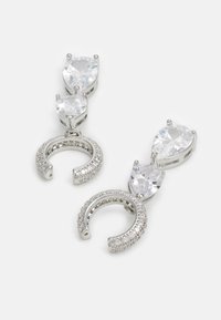 Boucles d'oreilles en métal argenté avec deux cristaux transparents en forme de goutte d'eau surmontés d'un motif de fer à cheval orné de petites pierres transparentes.