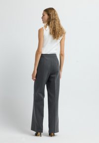 Pantalones gris con un diseño ajustado, que presentan una textura suave y perneras rectas, combinados con una blusa blanca sin mangas y tacones negros.