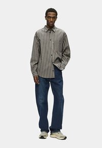 Srajca s črtami v sivi in bež barvi, z dolgimi rokavi in žepom na prsih, združena s temno modrimi kavbojkami s krojem ravnih hlačnic in supergami.