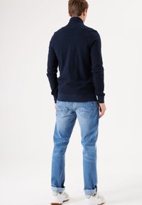 Maglione a maglia blu navy con colletto alto, indossato con jeans azzurri. Il maglione presenta polsini a costine e un design pulito e casual.