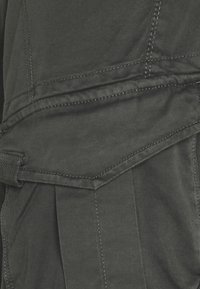 Gros plan sur un tissu gris foncé avec des coutures renforcées et un détail de poche à rabat.