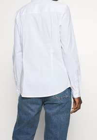 Weißes Langarmhemd mit spitzem Kragen, Knopfmanschetten und glatter Textur, kombiniert mit blauen Denim-Jeans.