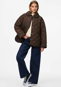 Gequilte bruine jacket met een rond kraag en drukknoopjes, gecombineerd met brede blauwe jeans en zwarte canvas sneakers.