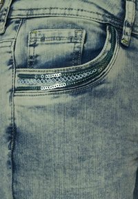 Jeans in denim azzurro chiaro caratterizzati da una piccola tasca frontale con una fila di paillettes blu brillanti lungo l'apertura. Effetto sfumato testurizzato su tutta la superficie.