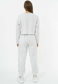 Grauer, cropped Sweatshirt mit langen Ärmeln, kombiniert mit passenden Jogginghosen. Das Material wirkt weich und strukturiert; elastische Bündchen sind sichtbar.
