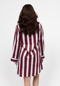 Abito camicia con maniche lunghe a righe verticali bordeaux e bianche. Presenta una vestibilità comoda, polsini alla lunghezza dei polsi e una texture del tessuto liscia.