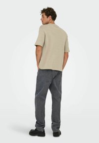 Lichtbruine, gestructureerde korte mouwen shirt met een ronde hals, gecombineerd met diepgrijze, losse jeans en zwarte chunky schoenen.