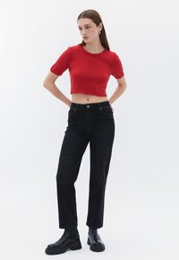 Cropped top in maglia rossa con maniche corte, abbinato a jeans in denim neri a vita alta e stivali neri chunky a caviglia. Outfit semplice e casual.