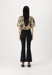 Bluse med blomstrende mønster i beige med puffermer, paret med svarte vide bukser og sandaler med tykk hæl, sett fra baksiden.