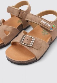 Sandalias de ante marrón con correa ajustable,Hebilla de metal y logo. Cuentan con una suela plana y un diseño con cortes para mayor transpirabilidad.