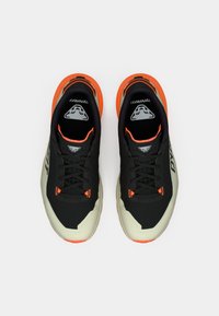 Μαύρα και μπεζ αθλητικά παπούτσια με διχτυωτό υλικό, φωτεινές πορτοκαλί λεπτομέρειες και υφή στη σόλα. Περιλαμβάνει σχέδιο με κορδόνια και λογότυπο στη γλώσσα.