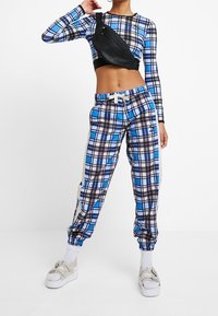 Blå och svart rutigt crop top med lång ärm, matchat med rutiga joggers i samma mönster med vita detaljer och en svart axelväska.