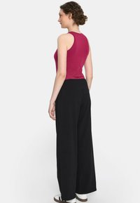 Różowa bluzka bez rękawów w połączeniu z czarnymi spodniami o szerokich nogawkach. Tkanina wydaje się gładka, o luźnym kroju i subtelnych detalach tekstury.