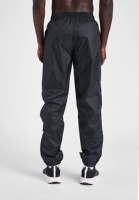 Svarta nylonträningsbyxor med resårmidja, smalnande ärmslut och sidofickor. Har en jämn textur och en lätt design.