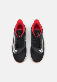 Černé sportovní boty s texturovaným svrškem, červenými akcenty uvnitř límce a bílým designem Nike swoosh na boční straně.