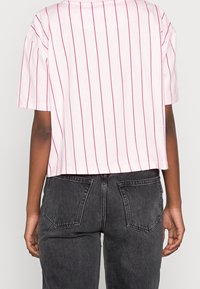 Skuren rosa t-shirt med tunna röda vertikala ränder, korta ärmar, rund halsringning, kombinerad med mörkgrå högmidjade jeans.