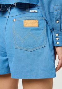 Ljusblå denimshorts med en läderpatch från Wrangler på bakfickan, kontrasterande sömmar och en klassisk stil med kort fåll.