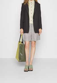 Musta bleiseri raidallisen vihreän ja kermaisen paidan päällä, yhdistettynä raidallisiin shortseihin, vihreisiin sandaaleihin ja vihreä-keltaiseen olkalaukkuun.