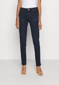 Jeans de mezclilla oscuros de corte slim con un diseño clásico de cinco bolsillos, que incluyen cierre de cremallera, botón y detalles de costura en contraste.