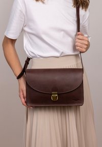 Braune Leder-Handtasche mit Klappenverschluss und goldenen Beschlägen. Verfügt über eine glatte Textur und einen langen, verstellbaren Trageriemen.