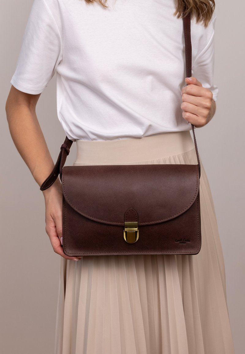 Braune Leder-Handtasche mit Klappenverschluss und goldenen Beschlägen. Verfügt über eine glatte Textur und einen langen, verstellbaren Trageriemen.