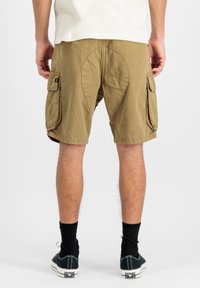 Pantaloni cargo color khaki, realizzati in tessuto leggero. Presentano due tasche laterali e un dettaglio a forma di ovale sulla parte posteriore. Indossati con sneakers basse.