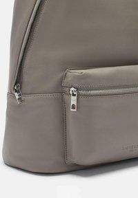 Mochila de cuero gris con una textura suave, bolsillo frontal con cremallera y acentos de hardware metálico. Diseño minimalista con líneas limpias.