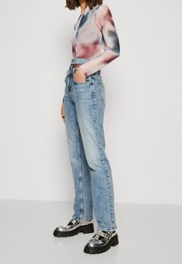 Långärmad, figursydd topp med ett färgglatt abstrakt mönster; ljusblå, högmidjade jeans; glittriga silverplattformsskor med svart sula.