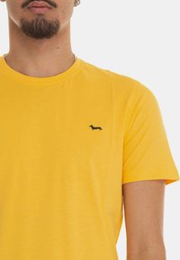 T-shirt giallo a maniche corte realizzato in cotone morbido, con un piccolo logo di un bassotto blu navy sulla parte sinistra del petto.