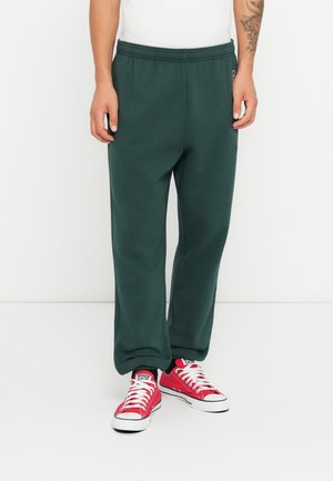 Pantalones jogger de algodón verde con una cintura elástica, con un ajuste relajado y bolsillos laterales, combinados con zapatillas rojas.
