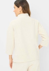 Cremefarvet sweatshirt med høj krave, trekvartærmer og afslappet pasform. Blødt, struktureret stof med synlige sting.
